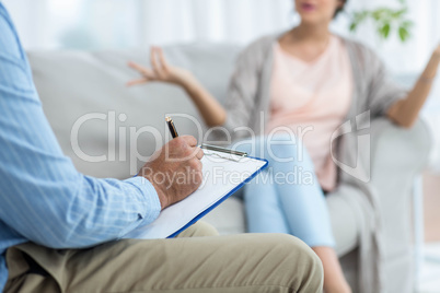 Doctor writing on clipboard while consulting pregnant woman