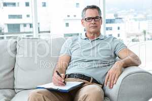 Man sitting on sofa and writing on notepad