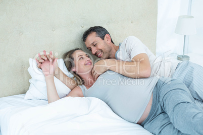 Expecting couple lying on bed and chatting