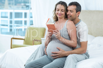 Expecting couple sitting on bed