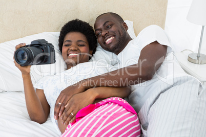 Pregnant couple lying on bed and looking photos in camera