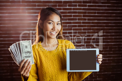 Smiling asian woman showing tablet and bank notes