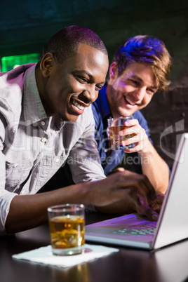 Two men having whiskey and using laptop at bar counter