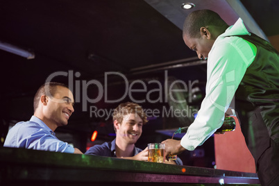 Bartender serving whiskey to two men at bar counter