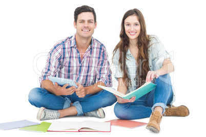 Happy couple studying with books and tablet while sitting on the