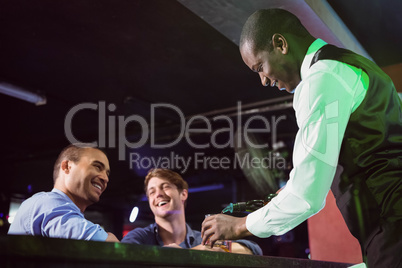 Bartender serving whiskey to two men at bar counter