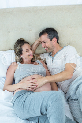 Expecting couple lying on bed and chatting