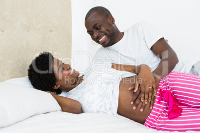 Man touching pregnant womans stomach while relaxing on bed