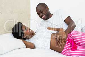 Man touching pregnant womans stomach while relaxing on bed