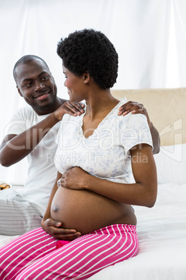 Man massaging pregnant womans shoulder on bed