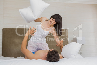 Woman playing pillow fight with man on bed