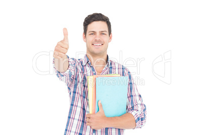 Portrait of smiling male student holding books and showing thumb