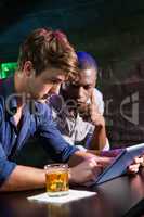 Two men having whiskey and using digital tablet at bar counter