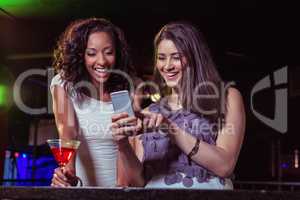 Two women looking at mobile phone and smiling at bar counter