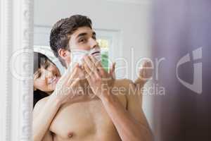 Young woman applying shaving cream on young mans face