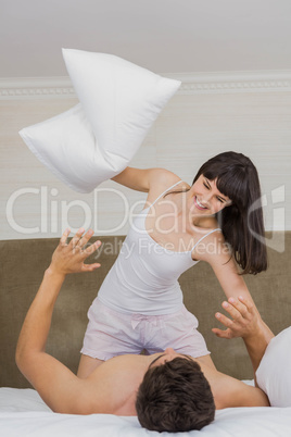Woman playing pillow fight with man on bed