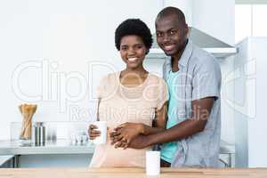 Pregnant couple embracing while having cup of coffee