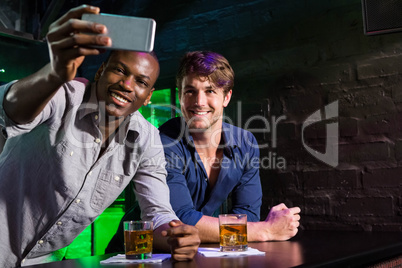 Two men taking a selfie on phone at bar counter