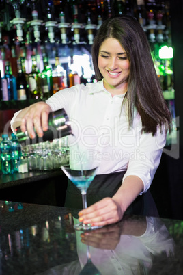 Pretty bartender pouring a blue martini drink in the glass