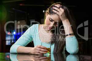 Depressed woman having whiskey at bar counter