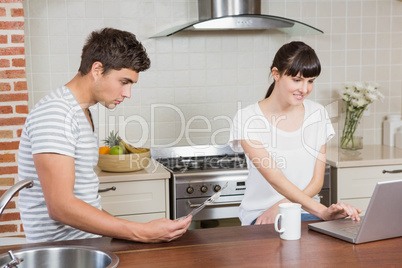 Woman using laptop and man reading newspaper