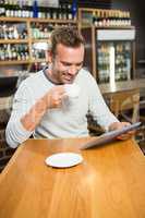 Handsome man using tablet computer and having a coffee