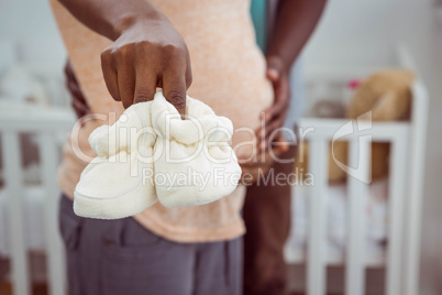 Pregnant couple holding white baby shoes