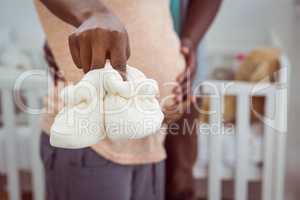 Pregnant couple holding white baby shoes