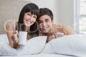 Young couple having cup of tea on bed