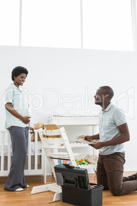 Pregnant woman looking at man fixing a baby chair