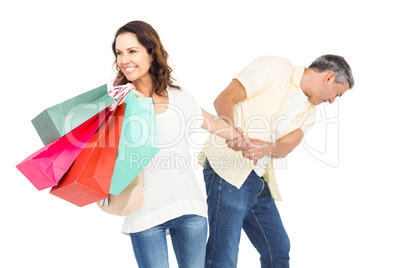 Smiling wife holding shopping bags with husband pulling her hand