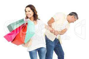 Smiling wife holding shopping bags with husband pulling her hand