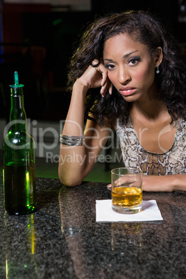 Depressed woman having whiskey at bar counter