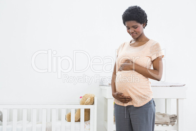 Pregnant woman standing near cradle and looking at her stomach