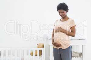 Pregnant woman standing near cradle and looking at her stomach