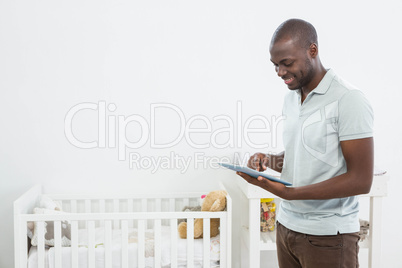 Smiling man standing next to a cradle and using digital tablet