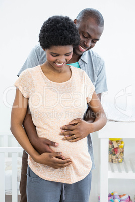 Pregnant couple embracing near cradle