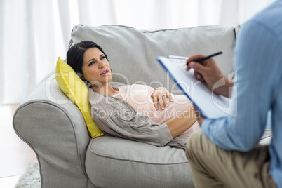 Doctor writing on clipboard while consulting pregnant woman