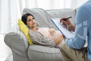 Doctor writing on clipboard while consulting pregnant woman