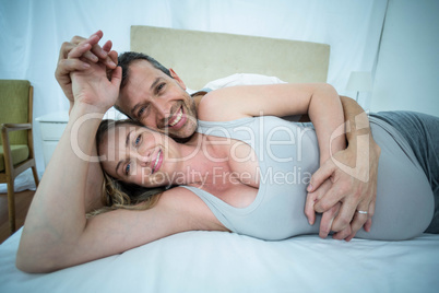 Expecting couple lying on bed and chatting