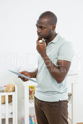 Thoughtful man standing next to a cradle and using digital table