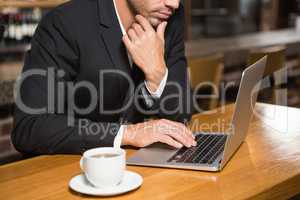 Thoughtful man using laptop and having a coffee