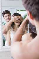 Man covering womans eyes while standing in front of bathroom mir