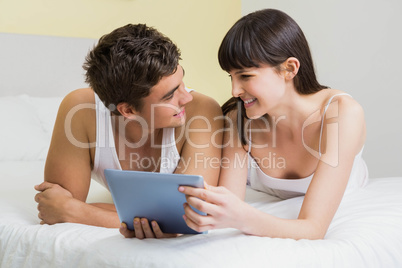 Couple using digital tablet on bed