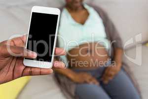 Man using phone and pregnant woman relaxing on sofa