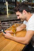 Handsome man using smartphone and having a beer