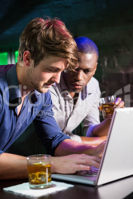 Two men having whiskey and using laptop at bar counter