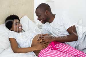 Man touching pregnant womans stomach while relaxing on bed