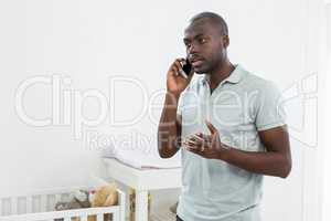 Smiling man standing next to a cradle and talking on mobile phon