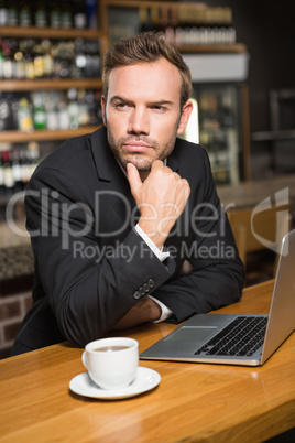 Thoughtful man using laptop and having a coffee